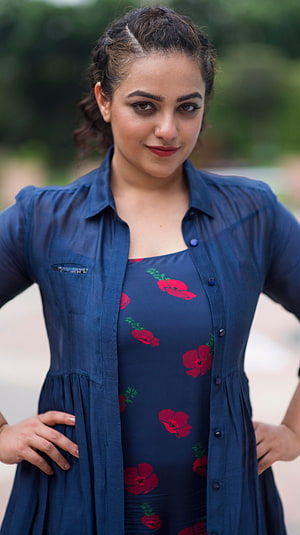 Nithya Menon in a navy floral dress with button-up shirt, posing outdoors with a confident smile HD phone wallpaper