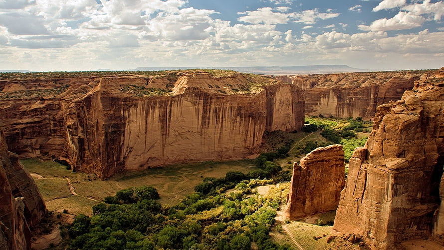 Dramatic Red Rock Canyon Walls With Lush Green Valley Floor Under Partly Cloudy Sky HD wallpaper