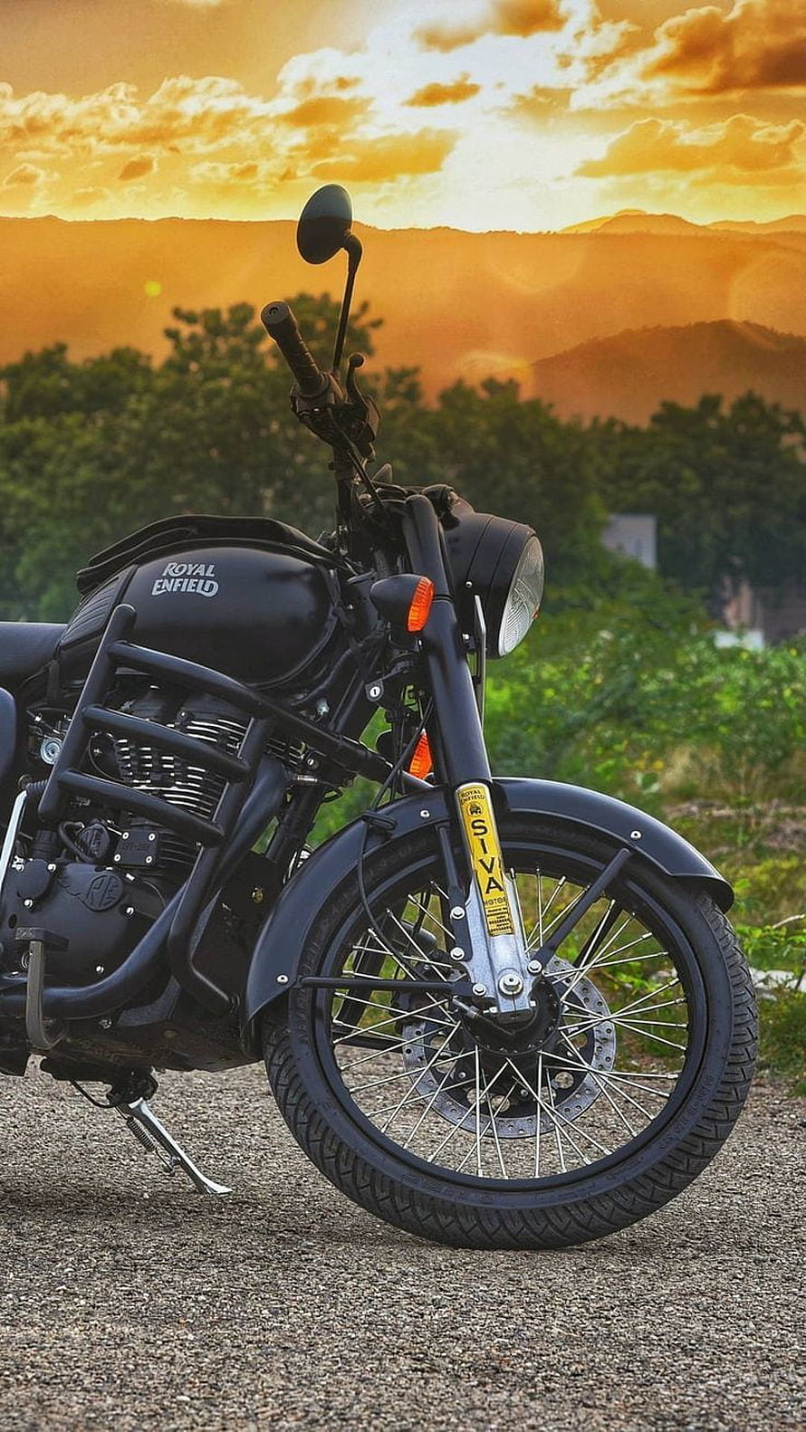 Black Royal Enfield Siva motorcycle parked on gravel with golden sunset and mountain backdrop HD phone wallpaper