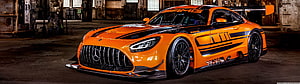 Orange Mercedes-AMG GT3 Race Car with Black Racing Livery in Industrial Warehouse Setting HD wallpaper
