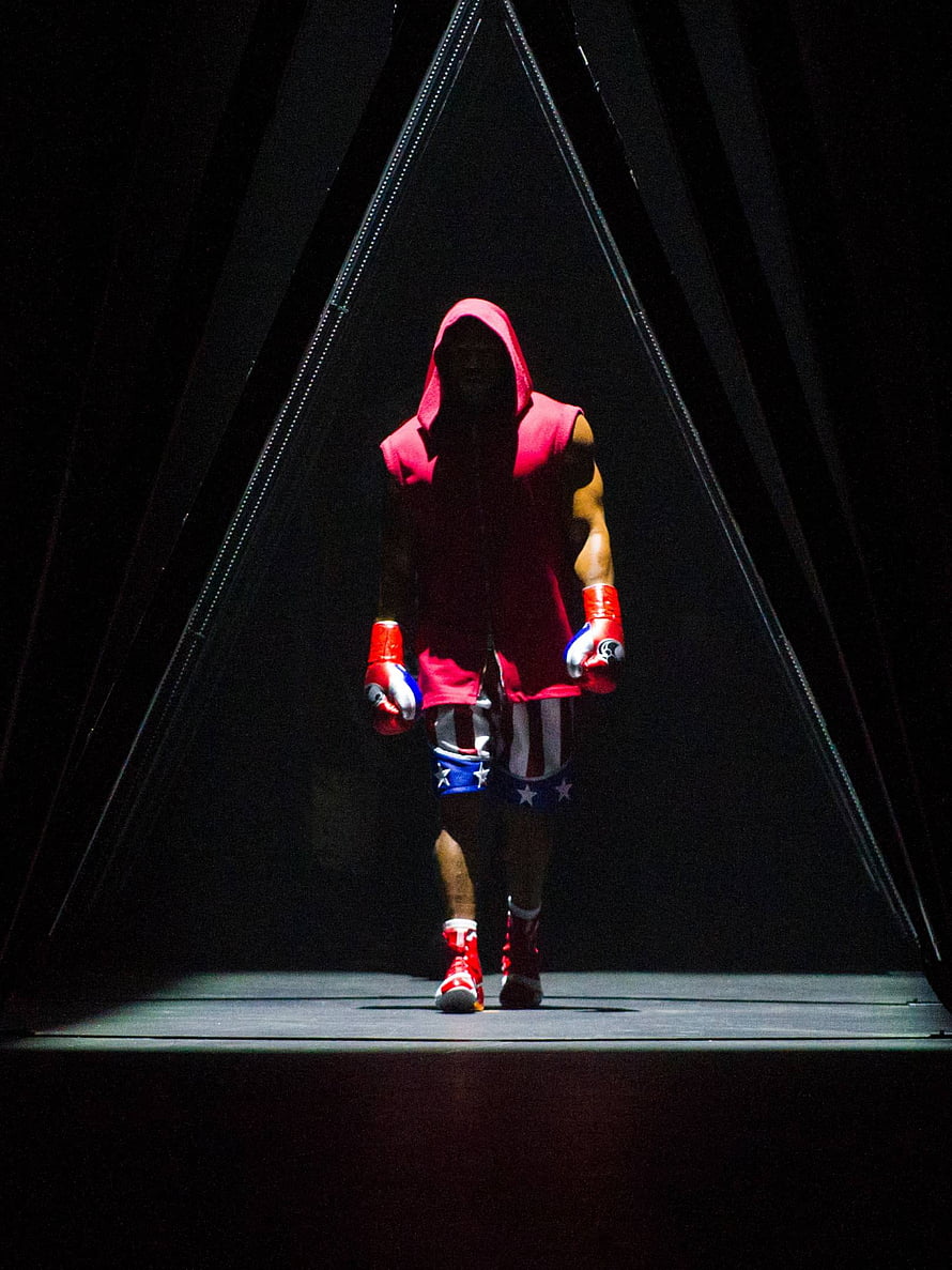 Adonis Creed in red hooded robe and boxing gloves walking through a dark spotlight tunnel HD phone wallpaper