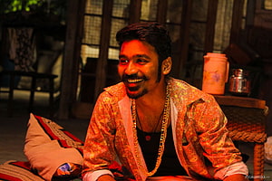 Dhanush in Maari wearing a patterned orange jacket and gold chain in a rustic interior HD wallpaper