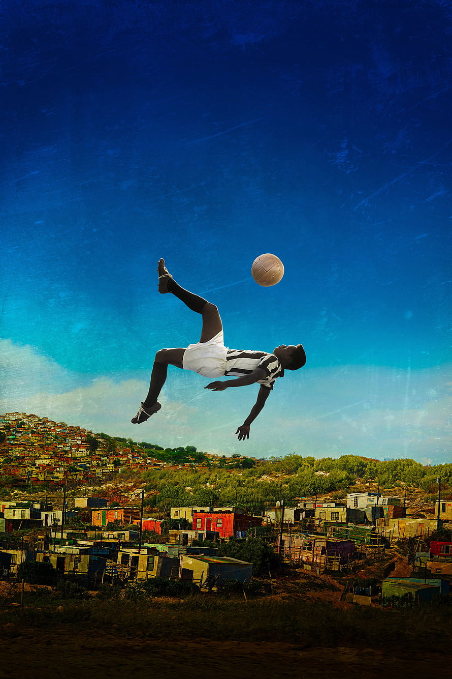Aerial Soccer Kick Over a Hillside Town Under a Deep Blue Sky HD phone wallpaper