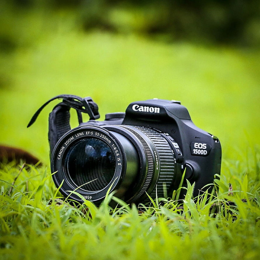 Canon EOS 1500D DSLR camera resting in vibrant green grass with shallow depth of field HD phone wallpaper
