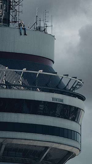 Drake Sitting on the Edge of a Tower Rooftop Under a Stormy Sky HD phone wallpaper