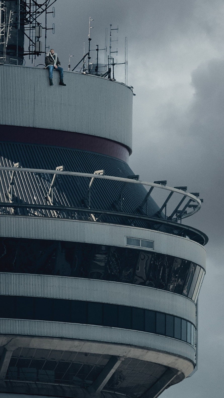 Drake Sitting on the Edge of a Tower Rooftop Under a Stormy Sky HD phone wallpaper
