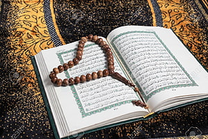 Open Holy Quran with wooden prayer beads resting on ornate patterned fabric HD wallpaper