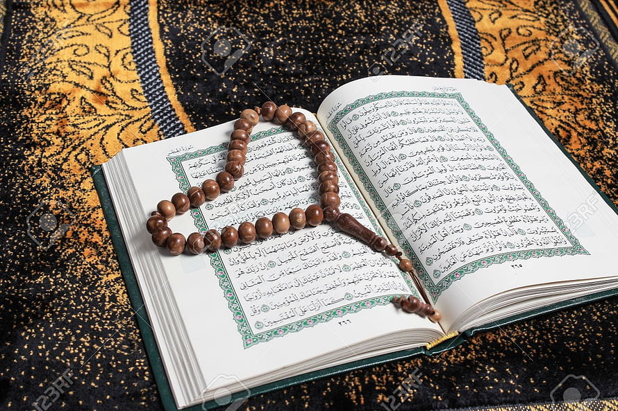 Open Holy Quran with wooden prayer beads resting on ornate patterned fabric HD wallpaper