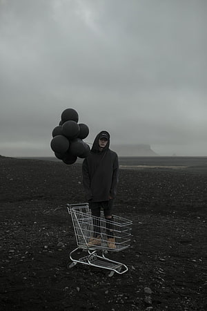 NF in dark hoodie with black balloons and shopping cart in desolate landscape HD phone wallpaper