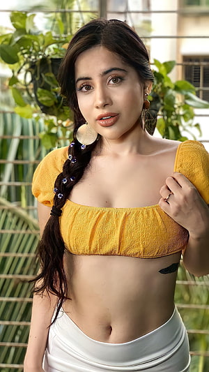 Urfi Javed in a mustard yellow crop top and white skirt with a side braid and large hoop earrings HD phone wallpaper