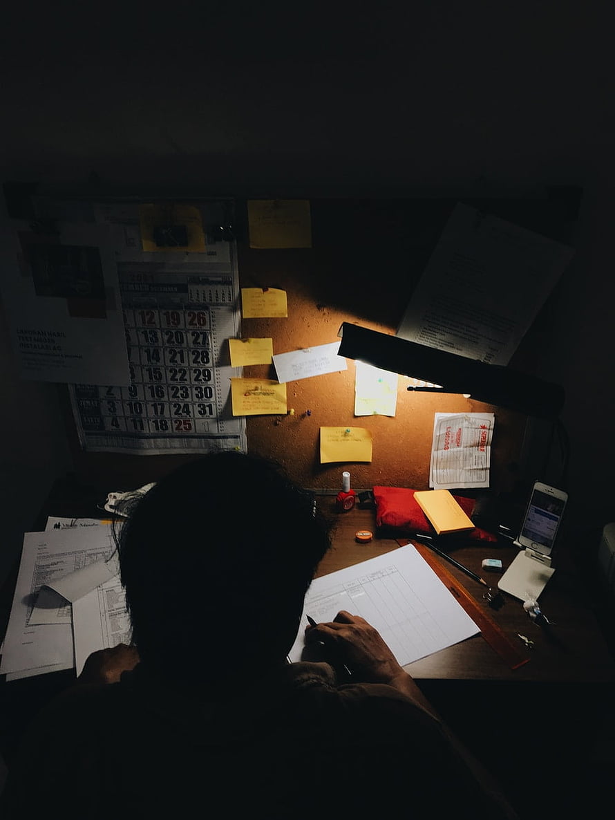 Silhouette of a Student Working at a Cluttered Desk Under a Single Lamp in a Dark Room HD phone wallpaper