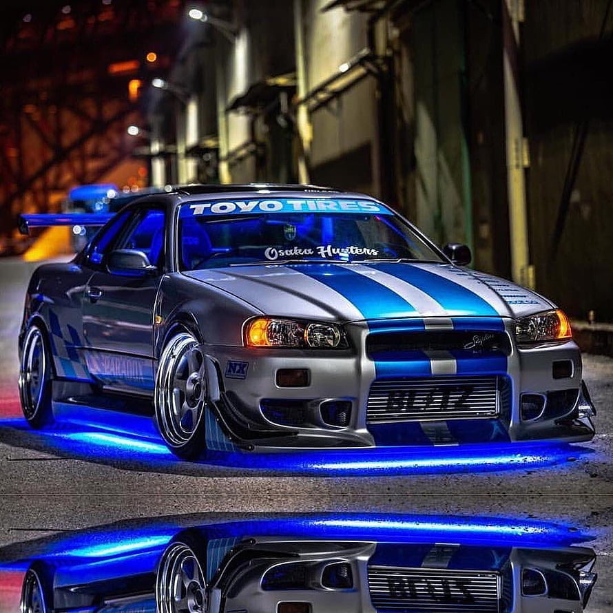 Nissan Skyline R34 GT-R with Blue Underglow and Racing Stripes in Night Street Scene HD phone wallpaper