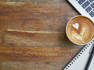 Flat lay of a latte with heart art on a rustic wooden desk beside a notebook and laptop HD wallpaper