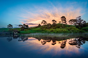 Serene Lake Reflection at Sunset with Rolling Green Hills and Scattered Trees HD wallpaper