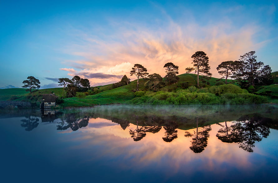 Serene Lake Reflection at Sunset with Rolling Green Hills and Scattered Trees HD wallpaper