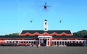 Indian Military Academy Dehradun with helicopters flying over the historic red and white building HD wallpaper