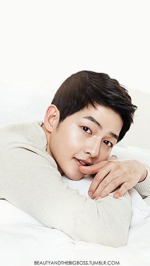 Song Joong Ki in a Soft Cream Knit Sweater Lying on White Bedding HD phone wallpaper