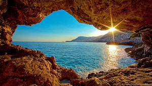 Sunlit Sea View Framed by Rocky Cave Arch and Coastal Cliffs HD wallpaper