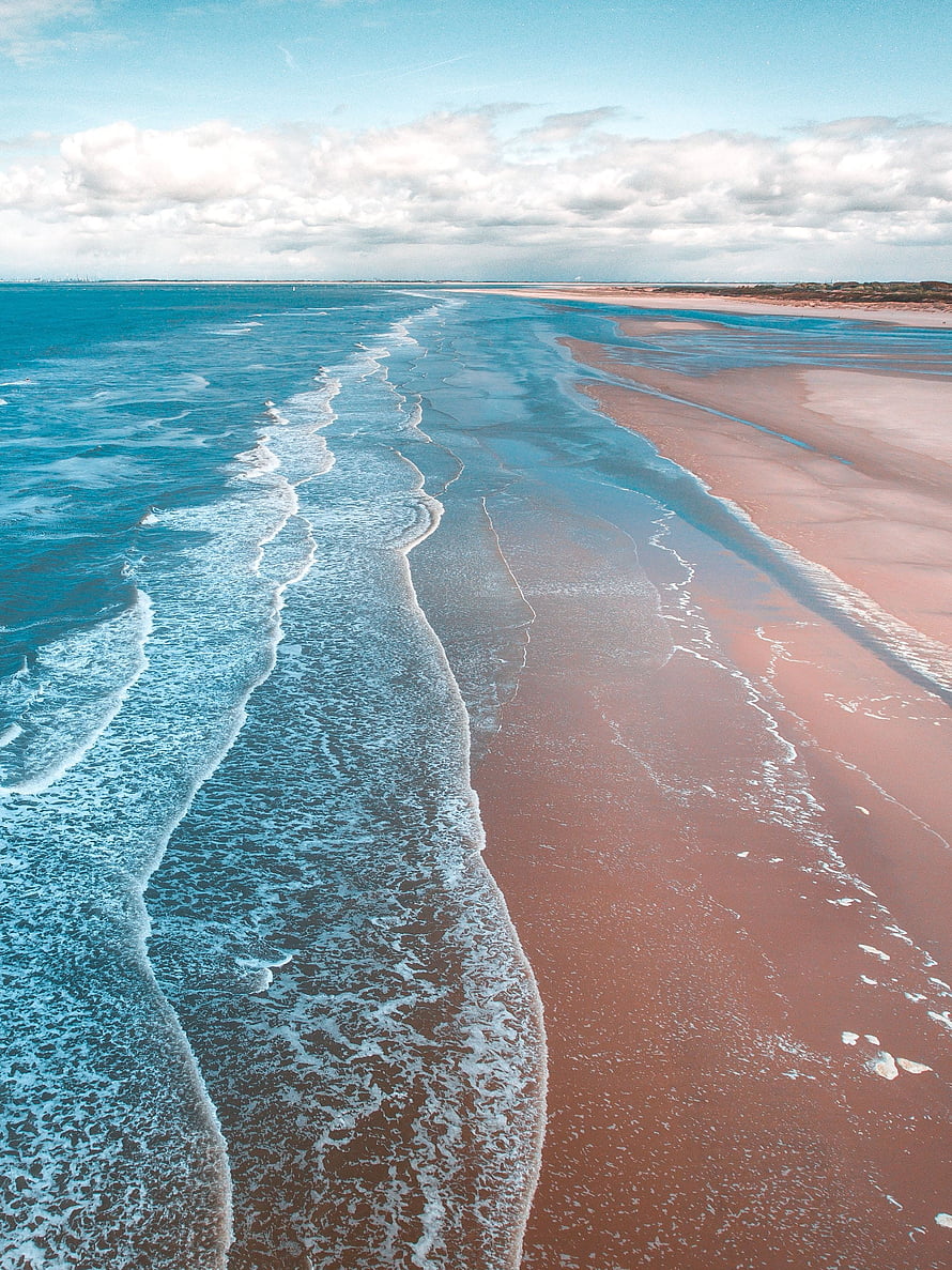 Aerial View of Turquoise Ocean Waves Rolling onto a Wide Sandy Beach Under a Partly Cloudy Sky HD phone wallpaper