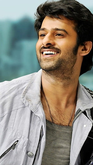 Prabhas smiling portrait in light jacket and grey t-shirt with soft teal background HD phone wallpaper
