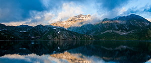 Serene Alpine Lake with Mountain Reflections Under Dramatic Clouds HD wallpaper