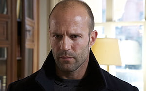 Jason Statham in a dark coat with a serious expression in an indoor setting HD wallpaper