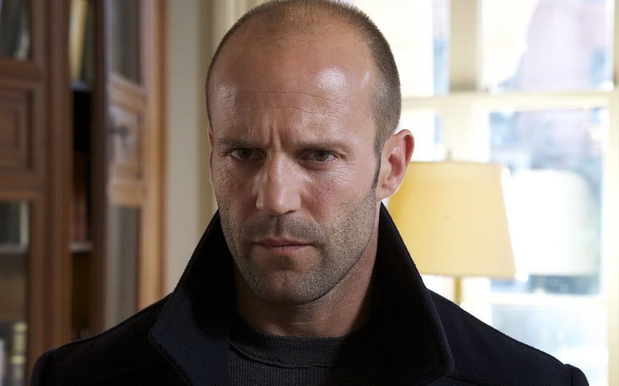 Jason Statham in a dark coat with a serious expression in an indoor setting HD wallpaper