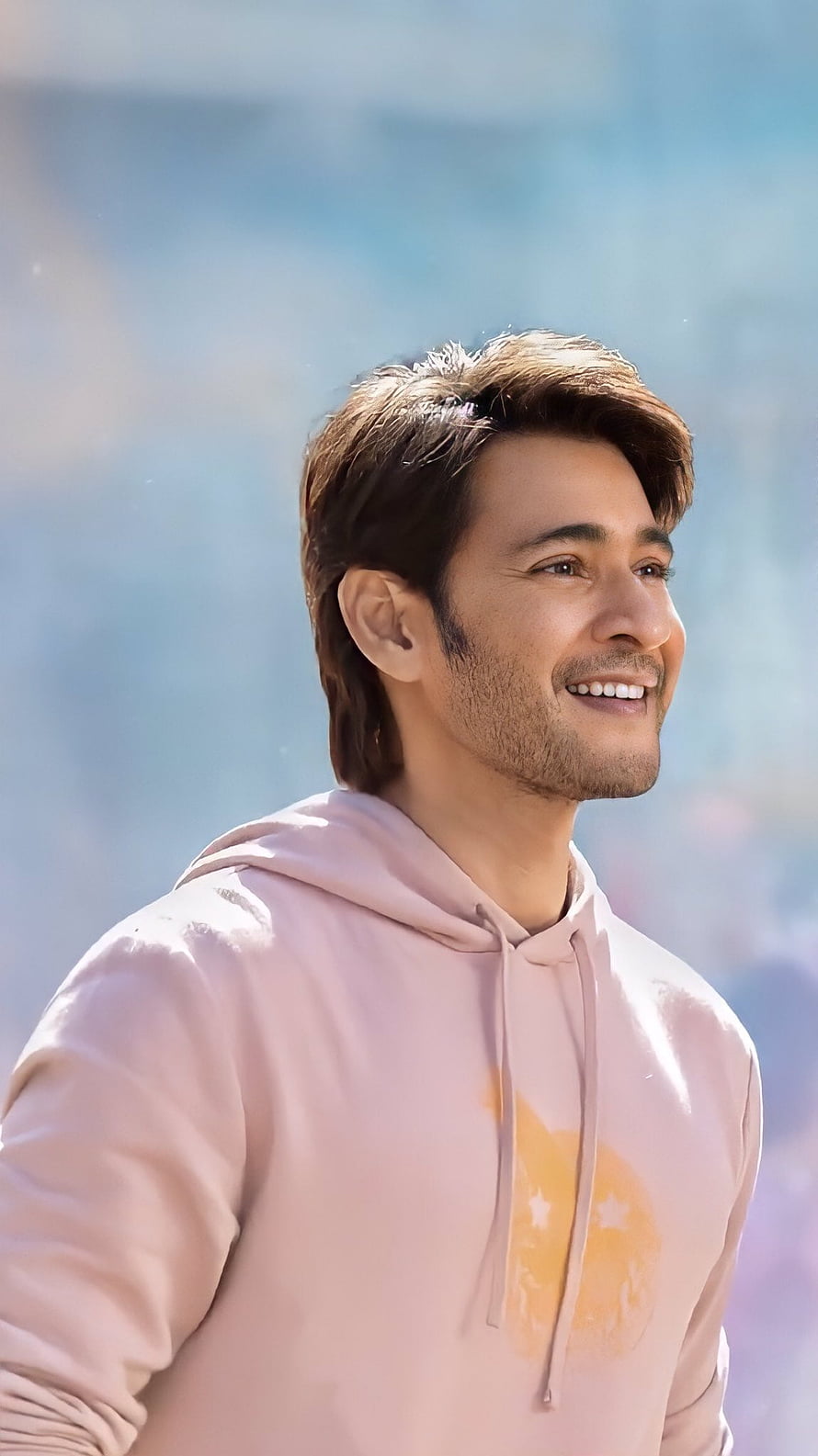 Mahesh Babu in a soft pink hoodie with a warm smile against a bright blue sky HD phone wallpaper