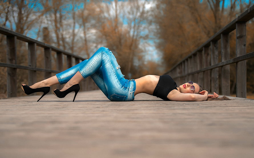Woman in blue jeans and black heels lying on a wooden bridge walkway HD wallpaper