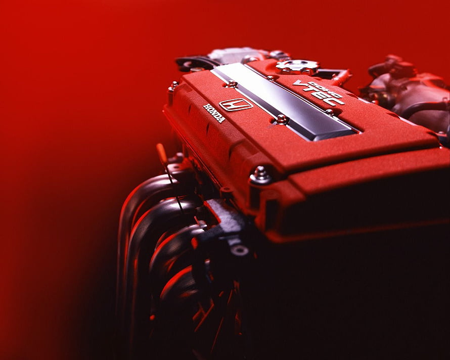 Close-up of a red Honda VTEC engine block with exhaust headers against a deep red background HD wallpaper
