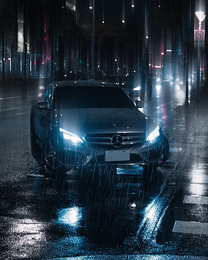 Black Mercedes-Benz sedan parked on a wet city street at night with heavy rain and glowing headlights HD phone wallpaper
