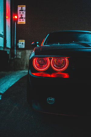 Rear View of a Black Muscle Car with Glowing Red Taillights on a Dark City Street at Night HD phone wallpaper