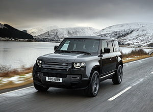 Land Rover Defender V8 110 Driving on a Scenic Road Beside a Snowy Lake HD wallpaper