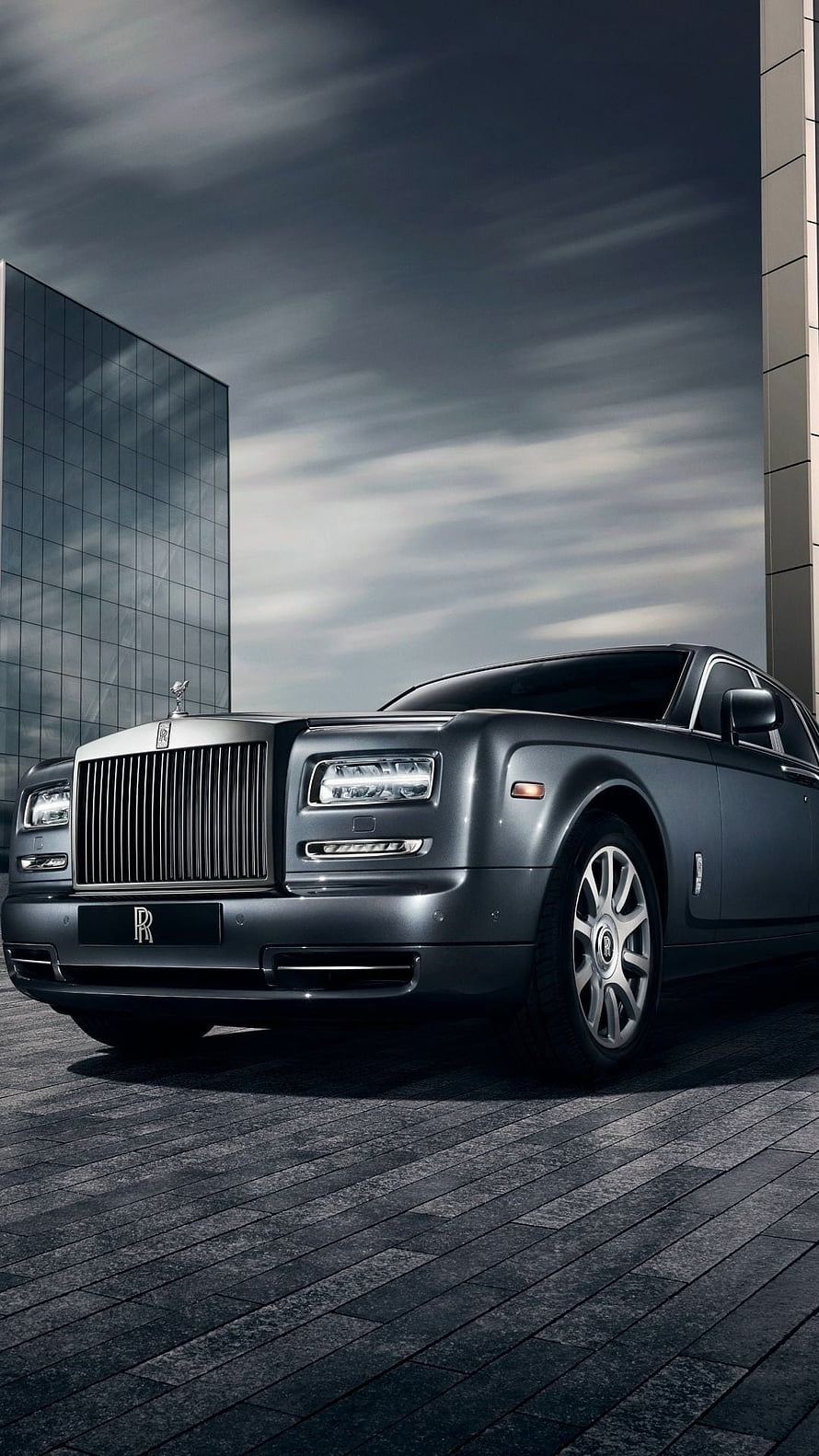 Rolls Royce Ghost luxury sedan parked on dark stone pavement under dramatic overcast sky HD phone wallpaper