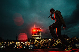 Travis Scott performing live on stage at a night concert with dramatic red lighting and a large crowd HD wallpaper