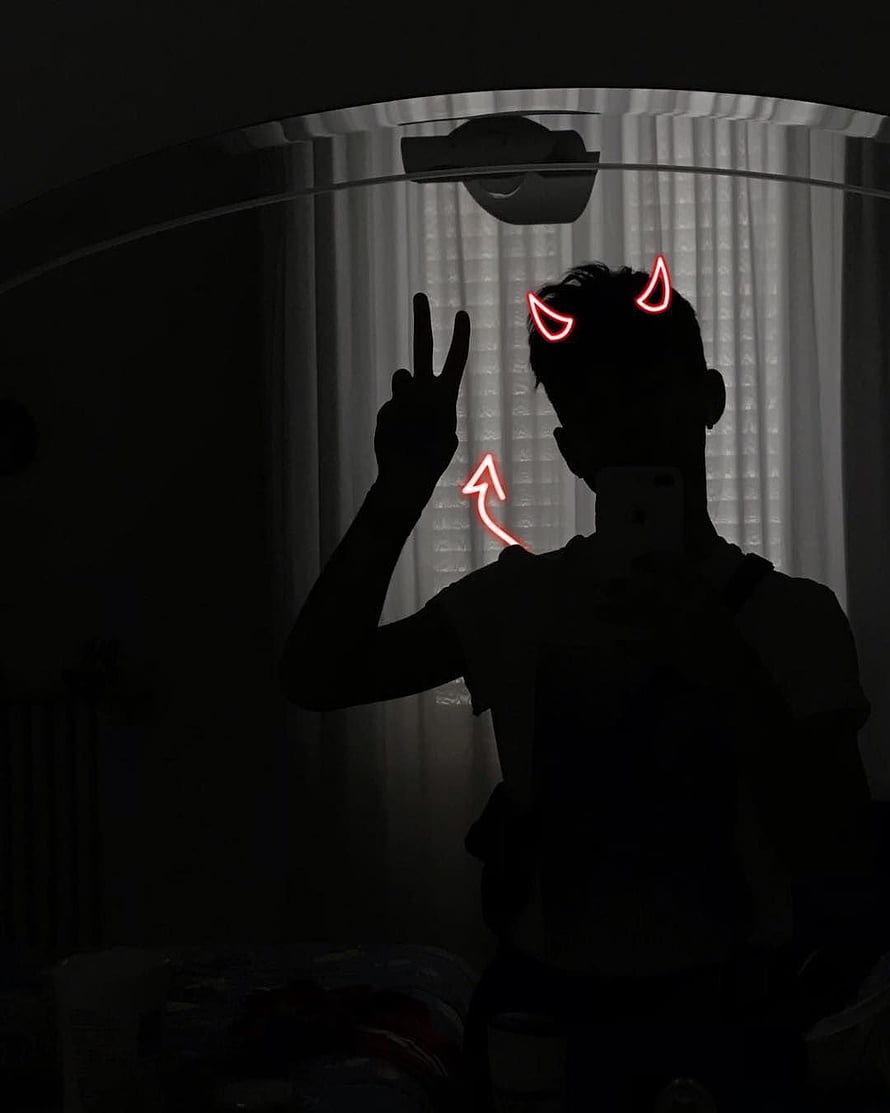 Silhouette of a person making a peace sign with glowing red devil horns and arrow overlay in a dark room HD phone wallpaper