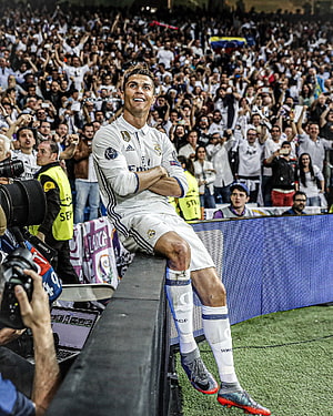 Cristiano Ronaldo in Real Madrid kit sitting on stadium barrier with cheering crowd behind HD phone wallpaper