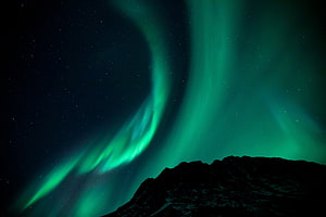 Vibrant Green Aurora Borealis Dancing Over a Dark Mountain Silhouette Under a Starry Night Sky HD wallpaper