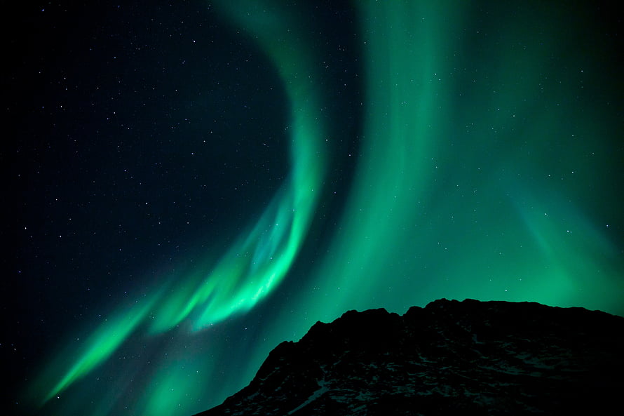 Vibrant Green Aurora Borealis Dancing Over a Dark Mountain Silhouette Under a Starry Night Sky HD wallpaper