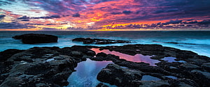 Vibrant sunset over rocky coastline with tide pools reflecting pink and orange sky HD wallpaper