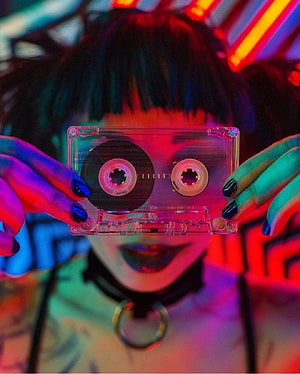 Neon-lit portrait of a person holding a clear cassette tape in front of their face HD phone wallpaper