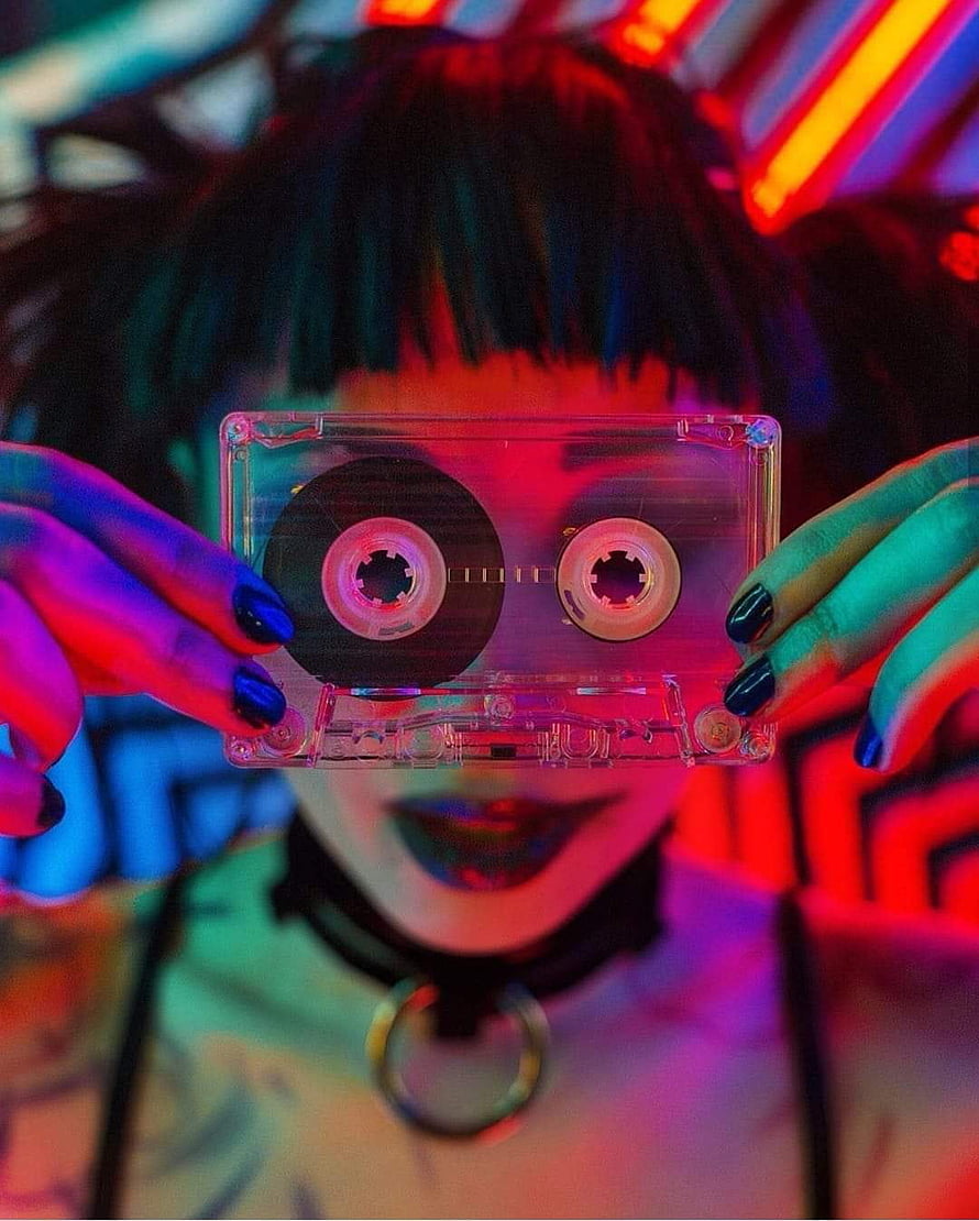 Neon-lit portrait of a person holding a clear cassette tape in front of their face HD phone wallpaper