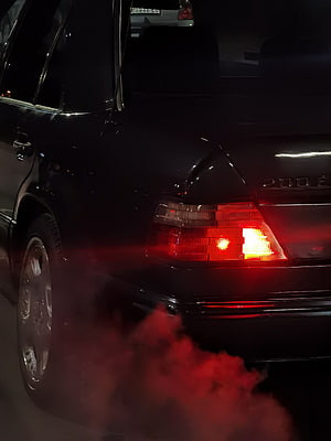 Rear View of a Black Mercedes-Benz W124 200E with Glowing Taillights and Red Smoke HD phone wallpaper