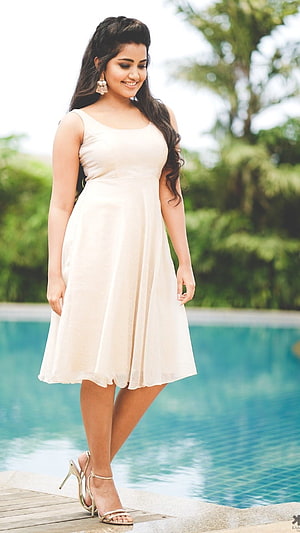 Anupama Parameswaran in a cream dress by a tropical pool HD phone wallpaper