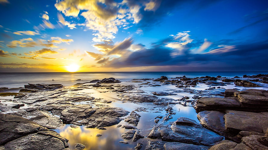 Golden sunset over a rocky ocean shoreline with dramatic clouds and water reflections HD wallpaper