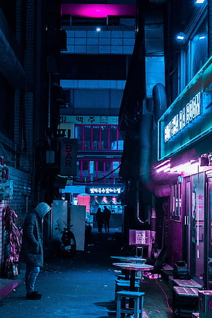 Neon-lit urban alleyway at night with glowing signs and a lone figure in a hooded coat HD phone wallpaper