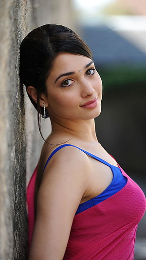 Tamanna Bhatia in a vibrant pink and blue saree leaning against a textured stone wall HD phone wallpaper
