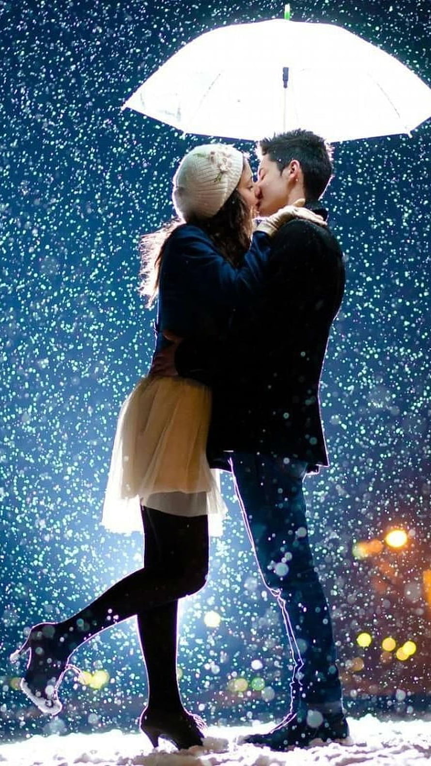 Romantic couple sharing a kiss under a white umbrella in falling snow at night HD phone wallpaper
