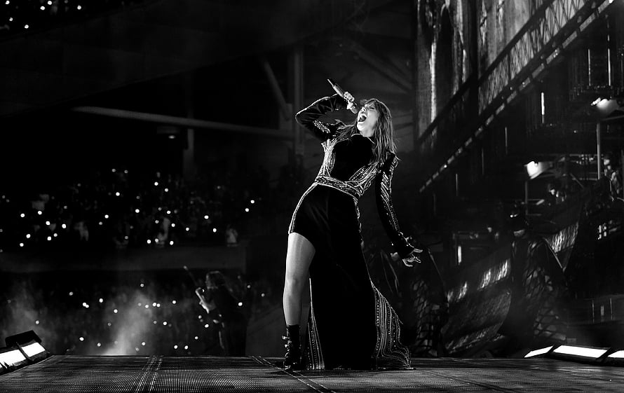 Taylor Swift performing on stage in a dramatic black gown during a live concert HD wallpaper