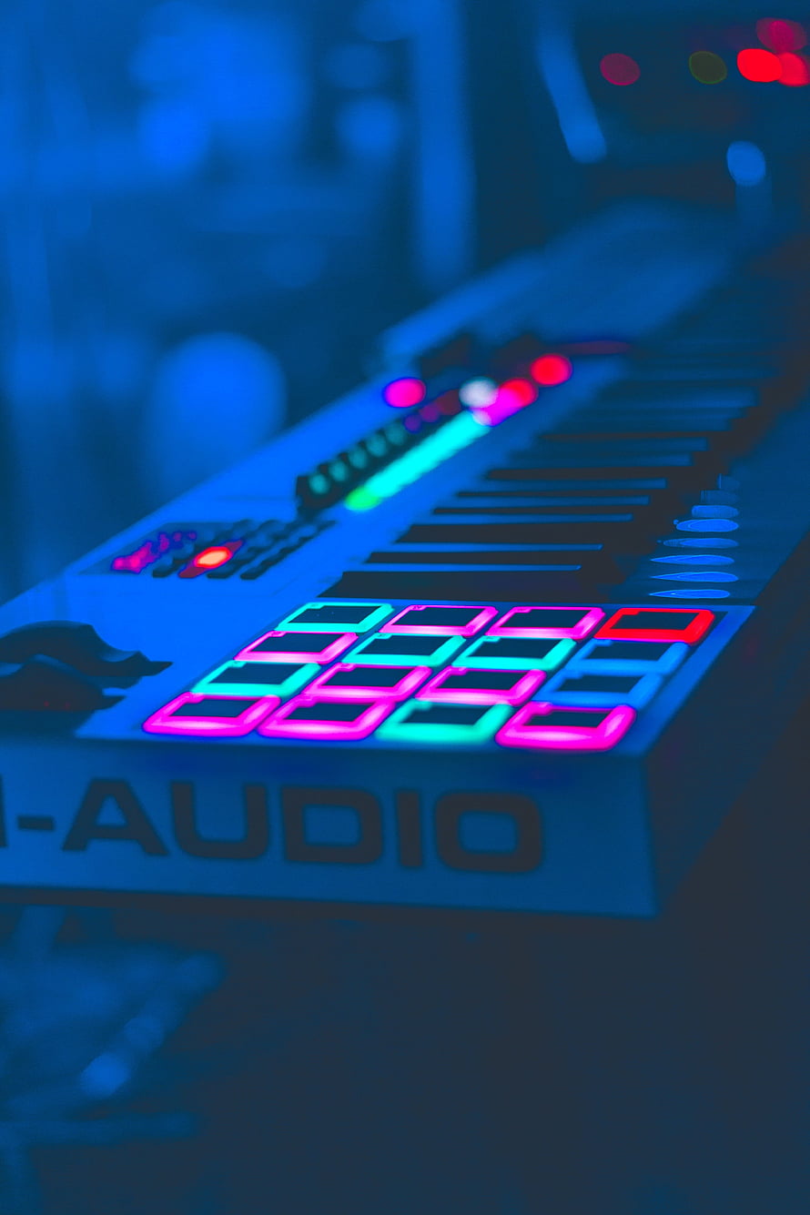 Neon-lit electronic music keyboard with glowing pads and keys in a dark studio setting HD phone wallpaper